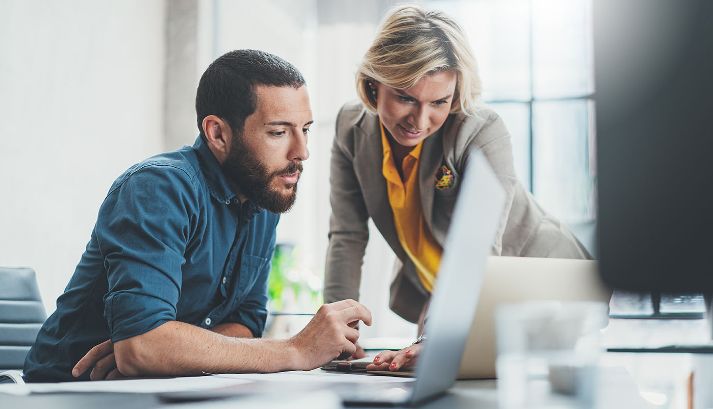 Frau und Mann sitzen vor Laptop und besprechen sich